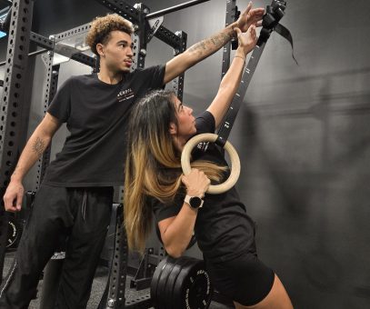 A male personal trainer is instructing a female client on how to use gymnastic rings for an exercise, showing how personal trainer certification enables varied workout instruction.